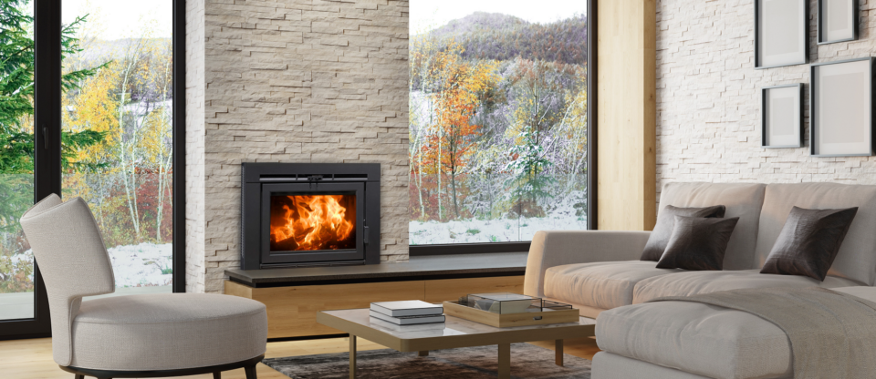 Modern living room with a stone fireplace, beige sofa, and snowy autumn view through large windows