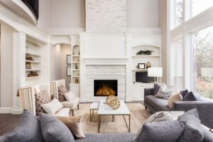 Modern living room with a white brick fireplace, beige seating, and large windows